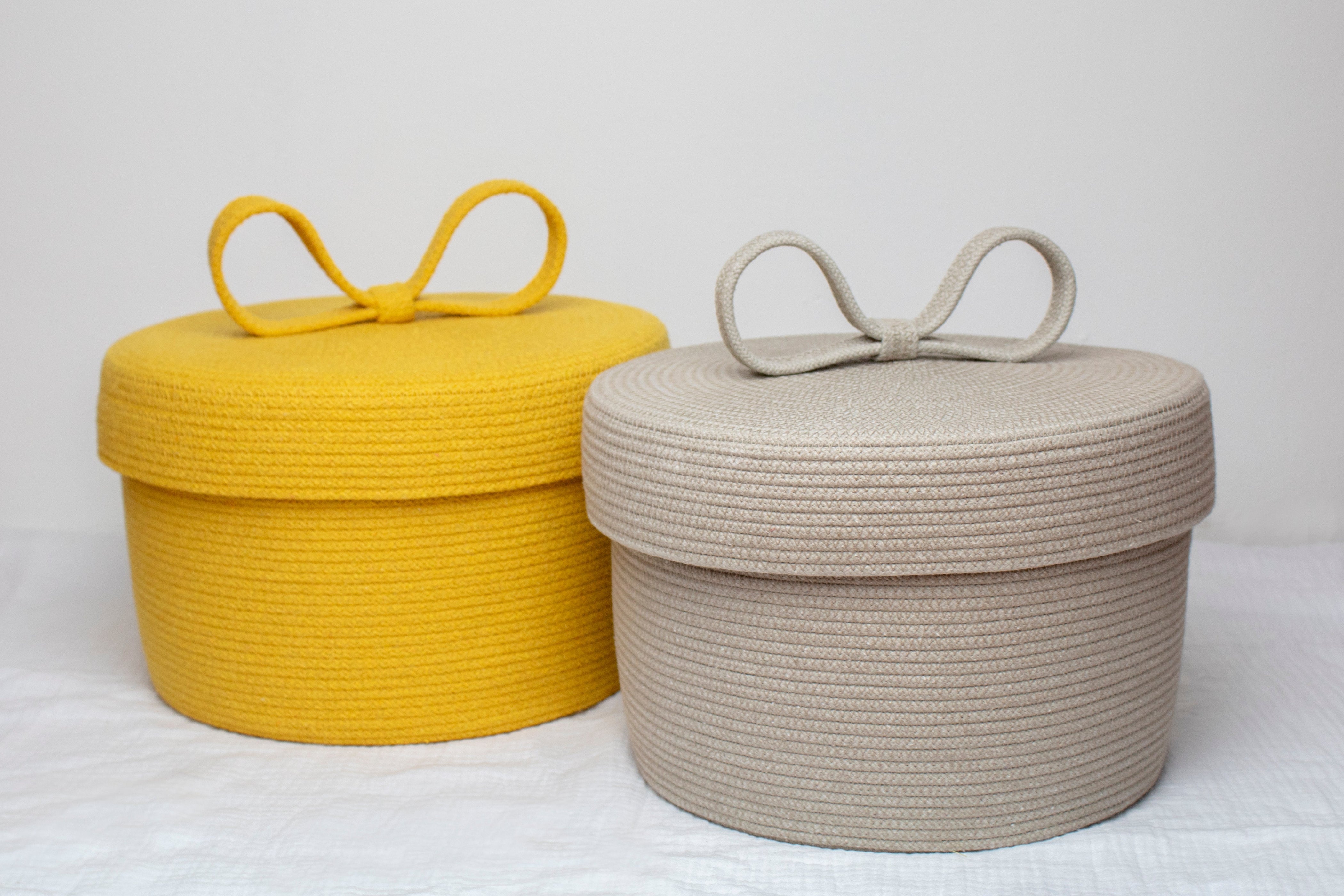 Two round woven baskets with lids, one yellow and one beige, on a white background.